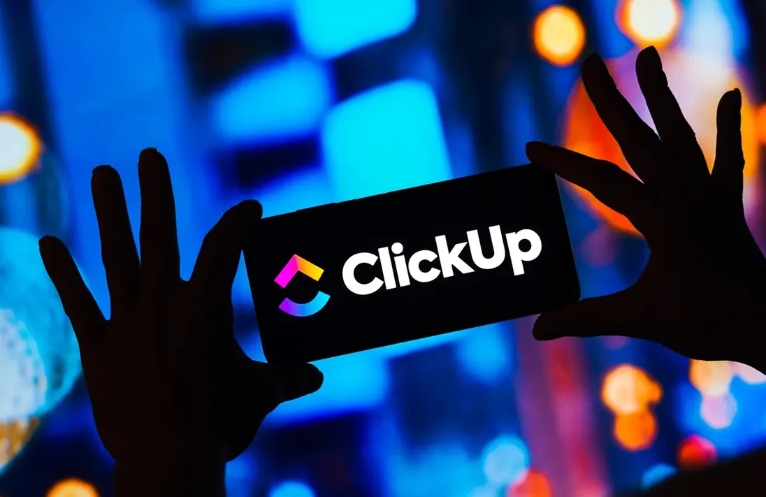 Marca do ClickUp exibida em painel de luz, com silhuetas de mãos à frente